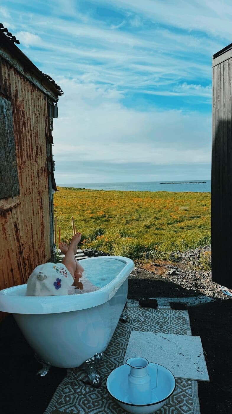 Gestur í köldu baðkari milli húsanna, sjórinn í baksýn